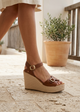Brown platform sandal worn on a stone floor with a plant in the background