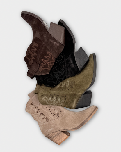 Stack of brown, black, and beige cowboy boots on a light gray background