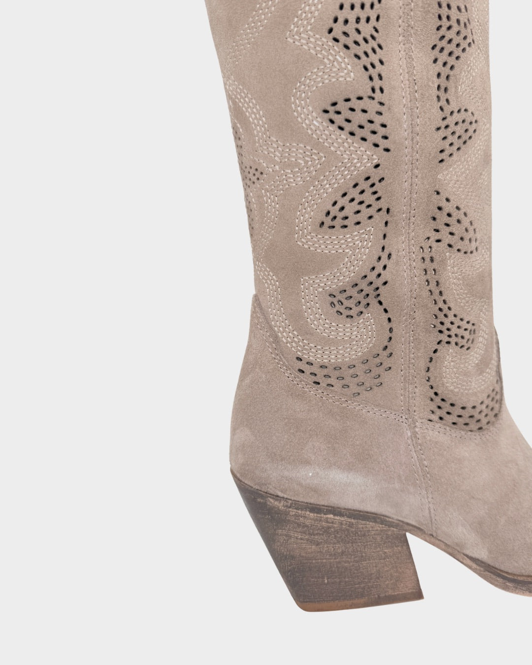 Close-up of a beige suede boot with decorative cut-out design on a light gray background